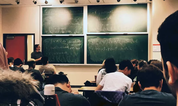A diverse group of students sitting in front of a professor and the blackboard of a college-level math class